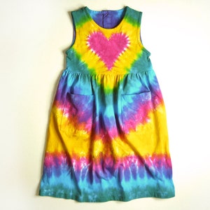 May include: A sleeveless tie-dye dress with a large pink heart in the center. The dress is yellow, blue, green, and purple.