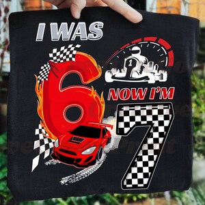 May include: Black t-shirt with a racing theme. Features the text "I WAS 6 NOW I'M 7" with a large red number 6 on fire, a red race car, and a checkered flag design. Includes a go-kart graphic.