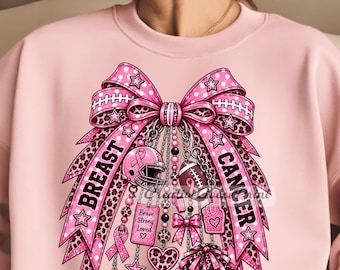 May include: A light pink sweatshirt featuring a large graphic of a pink bow with leopard print and polka dot patterns. The design includes a football helmet, a football, a pom-pom, and a tag with the text Brave Strong Loved and Breast Cancer.