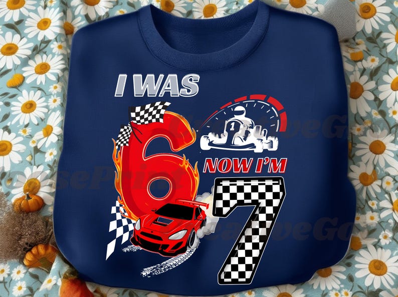 May include: Navy blue sweatshirt with a racing theme. Features the text "I WAS 6 NOW I'M 7" with a large red number 6 engulfed in flames, a red race car, and a checkered flag design. A speedometer and karting graphic are also included.