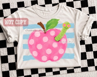 May include: A white short-sleeve t-shirt featuring a graphic of a pink apple with white polka dots, a green leaf, and a green worm wearing pink-rimmed glasses. The design is set against horizontal light blue stripes and includes the text NOT COPY.