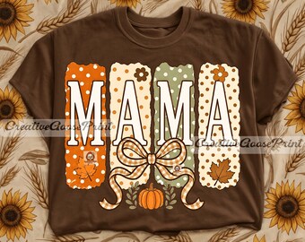 May include: A brown t-shirt featuring the word MAMA in large white letters. Each letter is set against a vertical rectangular panel with a polka dot pattern in orange, cream, and sage green. A beige gingham bow and a small orange pumpkin are below.