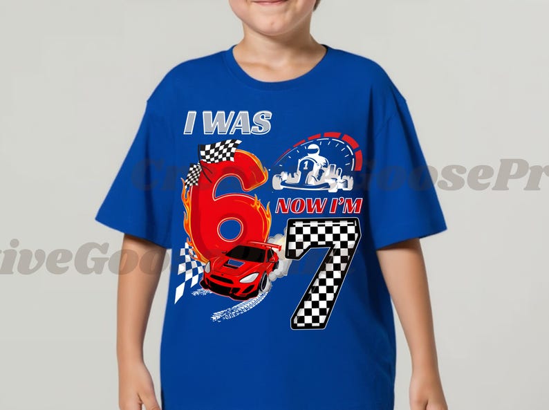 May include: Royal blue t-shirt with a racing design. The shirt displays the text "I WAS 6, NOW I'M 7" with a large red number 6 on fire, a red race car, and a checkered flag. A speedometer and a kart are also visible.