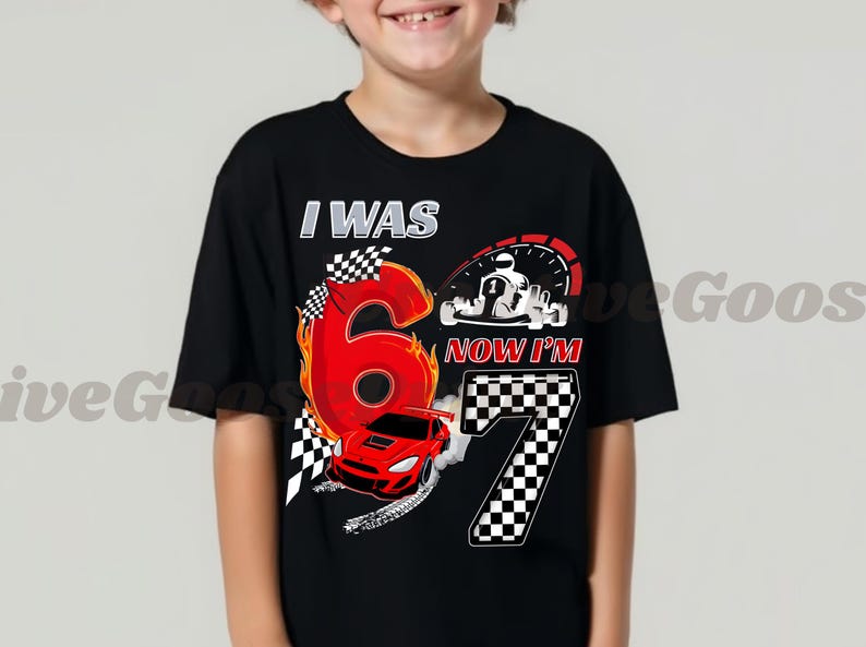 May include: Black t-shirt with a racing theme. The shirt features the text "I WAS 6 NOW I'M 7" with a large number 6 in red flames, a race car, and a checkered flag design. A speedometer and a race car are also visible.