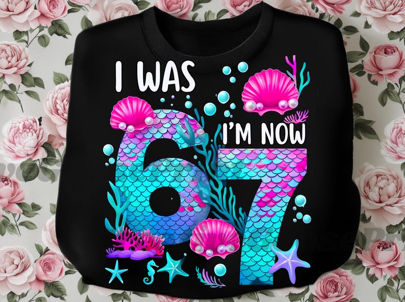 Puede incluir: Sudadera negra con el texto "I WAS 6, I'M NOW 7" en blanco. Los n&uacute;meros est&aacute;n dise&ntilde;ados con un patr&oacute;n de escamas de sirena en tonos azules y rosas, rodeados de conchas, corales y estrellas de mar.