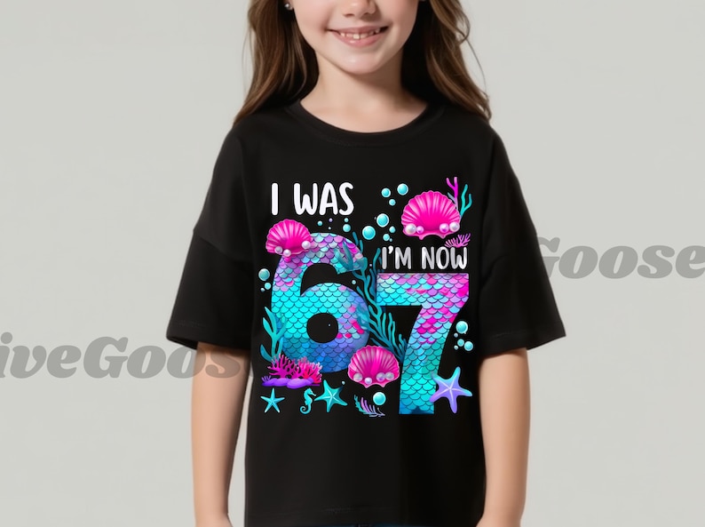 Puede incluir: Camiseta negra con un dise&ntilde;o de sirena. El gr&aacute;fico presenta los n&uacute;meros "6" y "7" en un patr&oacute;n de escamas de sirena, rodeados de conchas, estrellas de mar y el texto "I WAS 6, I'M NOW 7".