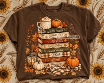 May include: A brown t-shirt featuring a graphic of a stack of books titled Autumn Stories, Pumpkin Spice, Fall Days, Leaves Falling, Sweater Weather, Crisp Air, and Harvest Blessings, topped with a mug and pumpkins, surrounded by autumn leaves.