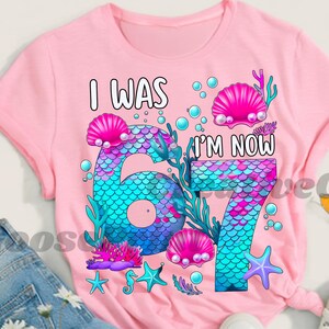 Puede incluir: Camiseta rosa con un dise&ntilde;o de sirena. El gr&aacute;fico presenta el texto "I WAS" encima de un n&uacute;mero grande "6" y "I'M NOW" encima de un "7", con escamas de sirena, conchas marinas y elementos acu&aacute;ticos.