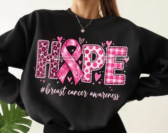 May include: A black long-sleeve sweatshirt featuring a graphic design that spells HOPE with a pink ribbon replacing the letter O. The letters have leopard, polka dot, and plaid patterns. Below the text is the hashtag #breast cancer awareness.