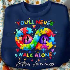 Op de afbeelding: Marineblauw sweatshirt met een kleurrijk puzzelstukontwerp in de vorm van een oneindigheidssymbool. De woorden "YOU'LL NEVER WALK ALONE" en "Autism Awareness" staan op de trui.