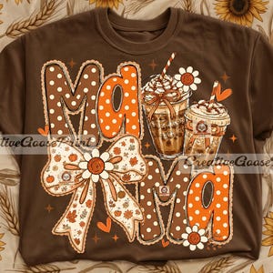 May include: A brown t-shirt featuring a graphic print with the word Mama in large polka-dot letters, two iced coffee drinks with whipped cream, a large decorative bow, and small flower accents in shades of orange, brown, and white.