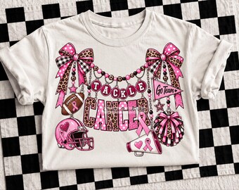 May include: A white t-shirt featuring a graphic print with the text TACKLE CANCER. The design includes pink football helmets, a football, a megaphone, pom-poms, and pennants with Go Team text, all accented with leopard print bows and pink ribbons.