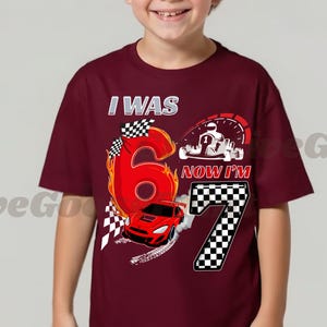May include: A maroon t-shirt with a racing theme. The shirt features the text "I WAS 6 NOW I'M 7" with a large number 6 in red flames, a red race car, and a checkered flag design. A go-kart graphic is also present.