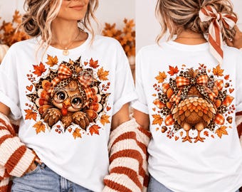 May include: A white t-shirt featuring a graphic of a turkey wearing glasses and a plaid bow, surrounded by autumn leaves, leopard print accents, and small hearts. The design is displayed on the front and back of the garment in this image.