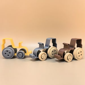 May include: Three toy tractors in yellow, blue-gray, and brown. Each tractor has a unique color scheme, with contrasting wheel colors. The tractors are designed with a simple, blocky aesthetic, suitable for children's play.