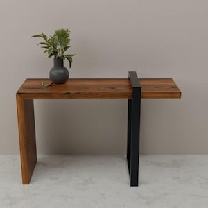 Könnte beinhalten: Ein moderner Konsolentisch aus Holz mit dunklem Finish und schwarzem Metallgestell. Eine kleine, dunkelgraue Vase mit Grün steht auf dem Tisch. Der Tisch ist etwa 122 cm lang.