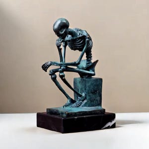 Może przedstawiać: Brązowa rzeźba przedstawiająca siedzącego szkieletu, opierającego podbródek na dłoni. Figura stoi na kwadratowym cokole, który stoi na czarnej marmurowej podstawie. Rzeźba ma zwietrzały, postarzany wygląd.
