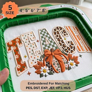 May include: An embroidery hoop containing white fabric with the word TEACH stitched in various patterns including orange flowers, polka dots, green checks, and leopard print. A pumpkin with a bow and autumn leaves is embroidered below.