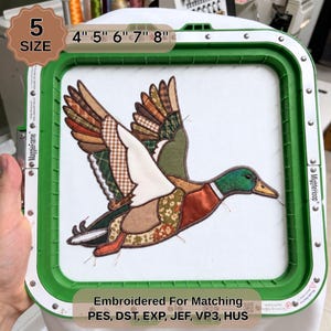 May include: A mallard duck embroidery design in a green embroidery hoop. The duck features patchwork-style fabric segments in brown, green, white, and orange patterns. Text includes 5 SIZE, 4" 5" 6" 7" 8", and Embroidered For Matching PES, DST, EXP, JEF, VP3, HUS.