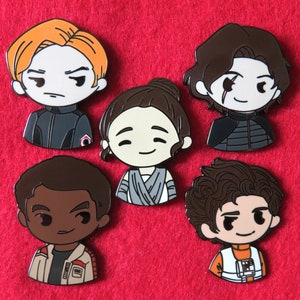 May include: Six enamel pins featuring characters from the Star Wars franchise. The pins are colorful and feature detailed illustrations of the characters. The characters include a young man with brown hair, a young woman with brown hair, a young man with black hair, a young man with brown hair, a young woman with brown hair, and a young man with black hair.