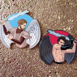 May include: Two enamel pins depicting angels, one with white wings and a blue sword, the other with black wings and a red sword.