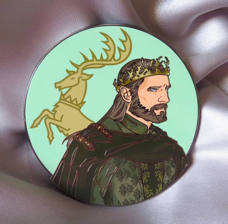 Puede incluir: Un pin de esmalte verde y dorado con el retrato de un hombre con corona y barba. El hombre lleva una t&uacute;nica con estampado verde y dorado. Un ciervo dorado est&aacute; en el fondo.