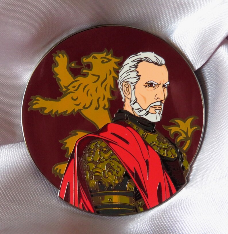 Puede incluir: Un pin de esmalte redondo con el retrato de un hombre con barba blanca y pelo gris. Lleva una capa roja sobre una armadura dorada. Un le&oacute;n dorado est&aacute; en el fondo.