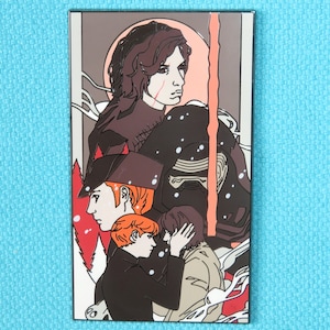 May include: A black and white enamel pin featuring characters from the Star Wars franchise. The pin depicts Kylo Ren, Rey, and Finn in a stylized illustration. The background is a red and orange gradient with a white snow effect.