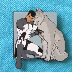 May include: A white and gray enamel pin featuring a cartoon soldier in a white and gray uniform hugging a gray wolf.