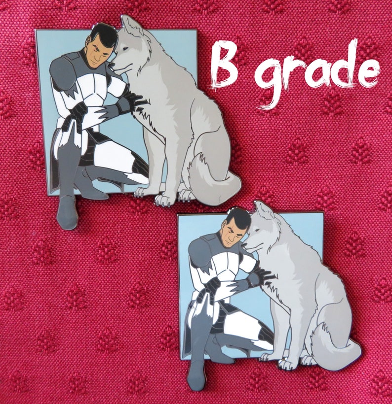 May include: Two enamel pins featuring a white wolf and a man in a white and black uniform. The man is kneeling and petting the wolf. The pins are set against a red fabric background. The text "B grade" is written in white on a black background.