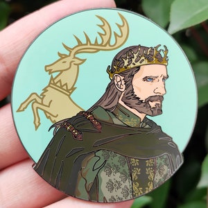 Puede incluir: Un pin de esmalte verde y dorado con un hombre barbudo que lleva una corona y una capa verde. El hombre est&aacute; de pie frente a un ciervo dorado con cuernos.