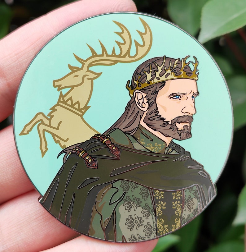 Puede incluir: Un pin de esmalte verde y dorado con un hombre barbudo que lleva una corona y una capa verde. El hombre est&aacute; de pie frente a un ciervo dorado con cuernos.