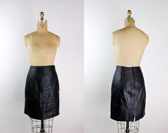 May include: A black leather skirt on a mannequin. The skirt is a knee-length design with a fitted shape. The leather has a subtle sheen. The mannequin is displayed on a wire stand against a white backdrop.