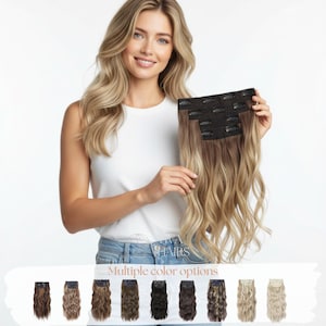 May include: A woman holding a set of wavy, clip-in hair extensions. The extensions transition from a dark brown to a light blonde color. The image also displays multiple color options for the hair extensions. The text "Kiva Hair" and "Multiple color options" are visible.