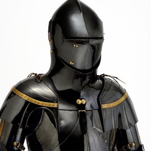 May include: A black, polished suit of armor with a helmet, shoulder guards, and chest plate. The armor has gold-colored trim and accents. The helmet has a visor and is designed to protect the face. The armor is likely made of metal.