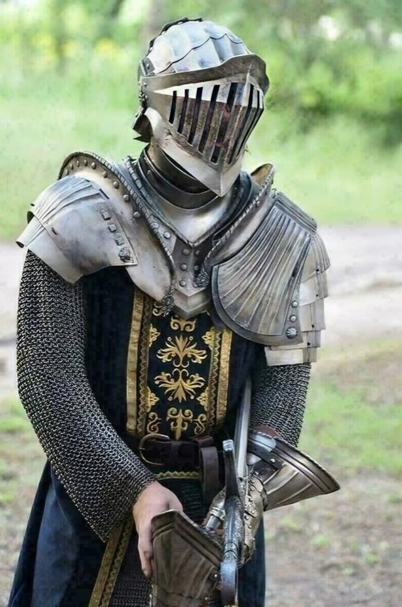 May include: A medieval knight in full armor, including a helmet with a visor, shoulder guards, and chainmail. The knight's attire features a black and gold patterned tunic and a sword. The background is a blurred green.