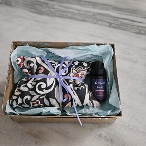 May include: A gift set in a decorative box. The box contains a patterned sachet tied with a lavender ribbon and a small bottle of essential oil. The sachet has a black background with floral and scroll designs in red, pink, and white.