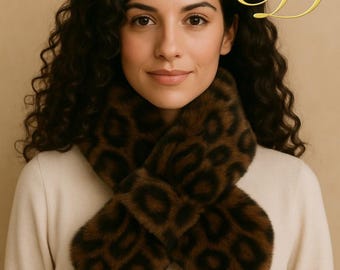 Puede incluir: Bufanda con estampado de leopardo marrón y negro. La bufanda está hecha de un material suave y afelpado y está envuelta alrededor del cuello. El fondo es de color beige liso.