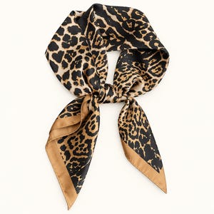 May include: A square scarf featuring a bold leopard print pattern in shades of black, tan, and brown. The scarf is tied in a knot at the centre, displaying a smooth, satin-like finish with solid tan borders along the edges of the fabric.