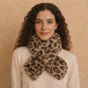 Puede incluir: Bufanda de piel sintética con estampado de leopardo. La bufanda tiene un fondo beige con manchas marrones. Está diseñada para llevarse alrededor del cuello y tiene una textura suave y afelpada.