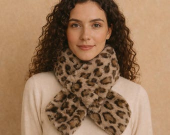 Puede incluir: Bufanda de piel sintética con estampado de leopardo. La bufanda tiene un fondo beige con manchas marrones. Está diseñada para llevarse alrededor del cuello y tiene una textura suave y afelpada.