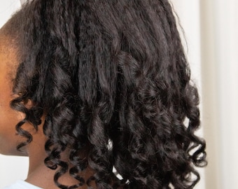 May include: Close-up of dark, curly hair styled with a white bow. The hair is styled in loose, defined curls. The person is wearing a light blue top. The text "Tumble Textures" is visible at the bottom of the image.