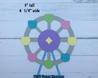 May include: A handmade paper die cut of a Ferris wheel. The Ferris wheel is 5 inches tall and 4 1/4 inches wide. It features a gray wheel with colorful gondolas in shades of blue, green, pink, and yellow. The center is purple with a yellow diamond. Text reads "CKS Paper Designs Handmade Die Cuts."