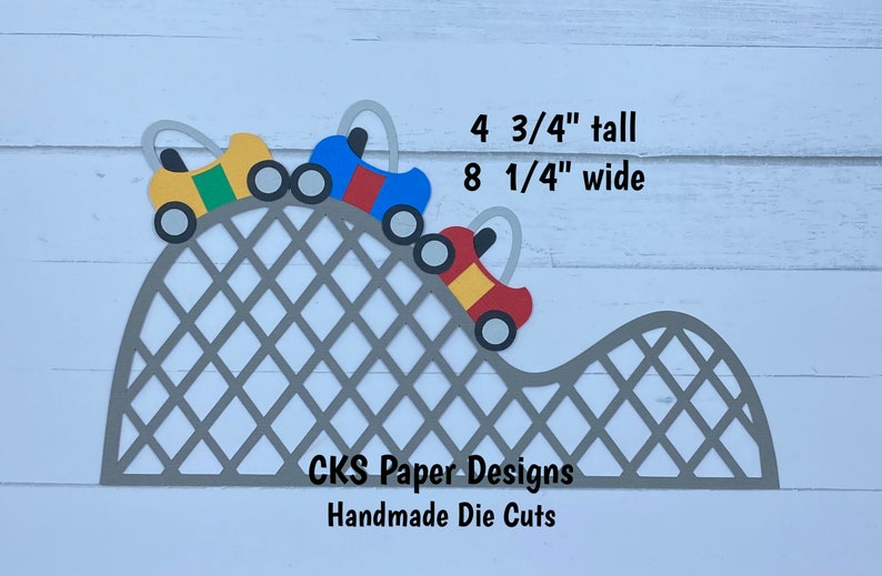 May include: Three paper die-cut cars in red, blue, and yellow colors driving up a gray paper roller coaster track. The track is 4 3/4 inches tall and 8 1/4 inches wide. CKS Paper Designs Handmade Die Cuts.