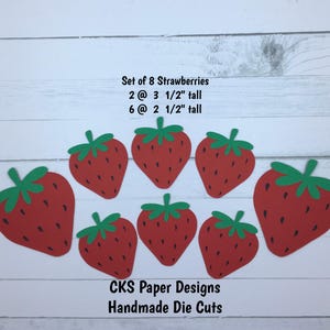 May include: Set of 8 red and green paper die cut strawberries.  There are 2 strawberries that are 3 1/2 inches tall and 6 strawberries that are 2 1/2 inches tall.  The text "Set of 8 Strawberries", "2@ 3 1/2" tall", "6@ 2 1/2" tall", "CKS Paper Designs", and "Handmade Die Cuts" is printed on a white wooden surface.