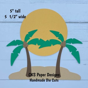 May include: A paper craft die cut set featuring two palm trees with coconuts and a yellow sun. The set is 5 inches tall and 5 1/2 inches wide. The text "CKS Paper Designs Handmade Die Cuts" is included on the craft paper.