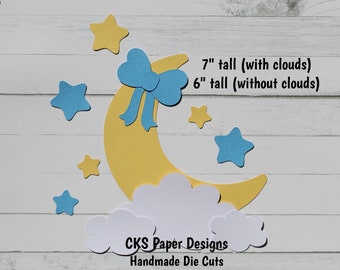May include: A yellow crescent moon with a blue bow on top, surrounded by white clouds and blue stars. The moon is 7 inches tall with clouds and 6 inches tall without clouds. The text "CKS Paper Designs Handmade Die Cuts" is at the bottom of the image.