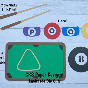 May include: A set of paper die cuts for a pool table themed craft project. The set includes a green pool table with a brown frame, a triangle rack, two brown cue sticks, four pool balls with the letters P, O, O, and L, and a black 8 ball. The die cuts are handmade and measure 2 1/2 inches, 1 5/8 inches, 5 3/4 inches, and 3 5/8 inches.