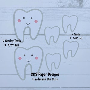 May include: Two white teeth with pink cheeks and a smiley face, and four plain white teeth, all cut from paper. The text "2 Smiley Teeth 3 1/2" tall" and "4 Teeth 1 7/8" tall" is printed below the teeth. The text "CKS Paper Designs Handmade Die Cuts" is printed below the teeth.