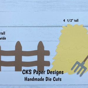 May include: A set of brown paper die cuts for crafting. The set includes a fence, a hay bale, and a pitchfork. The fence is 2 3/4 inches tall and 5 3/4 inches wide. The hay bale is 4 1/2 inches tall. The pitchfork is 4 1/4 inches tall. The text "CKS Paper Designs Handmade Die Cuts" is also included.